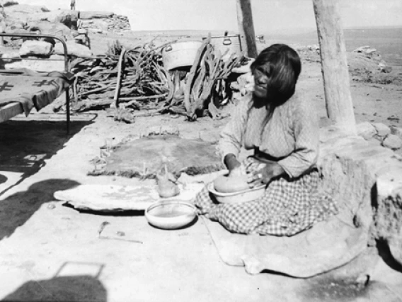 A Hopi woman sits on the ground in the beginning stages of making a pot.