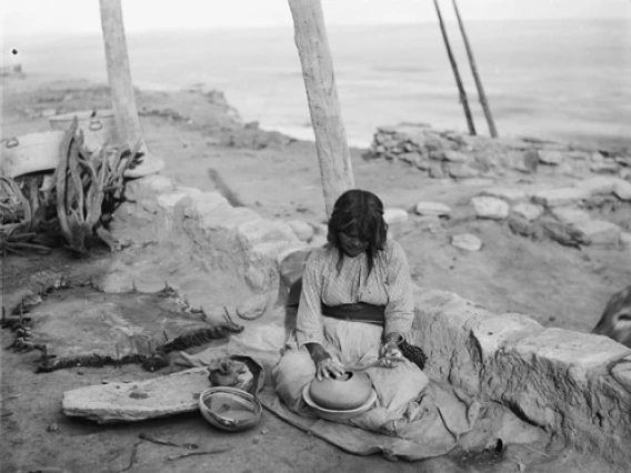 A Hopi woman sits on the ground in the beginning stages of making a pot.