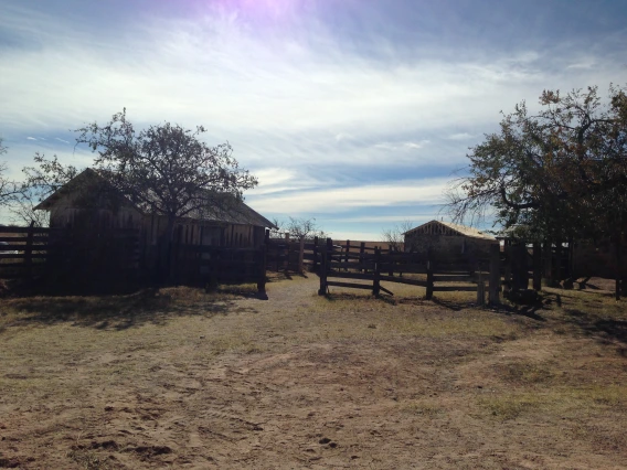 historic ranch setting in southern Arizona, showing two wooden structures behind a wooden fence on grassy land