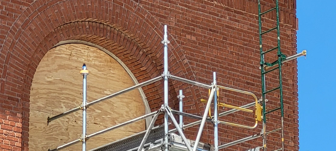 a window showing plywood covering where the glass used to be and scaffolding in front of it 