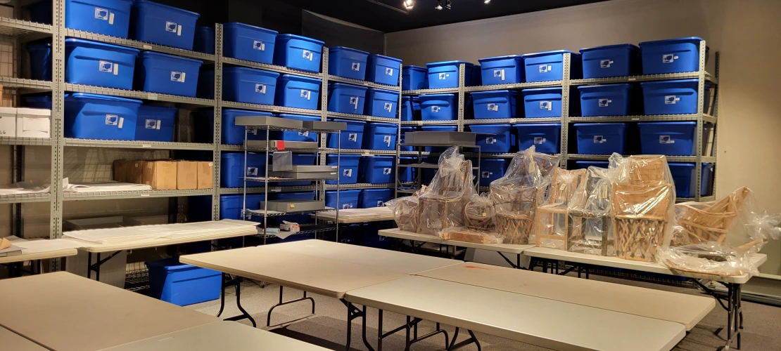 A room with shelving filled with blue tubs in the background and tables in the foreground.