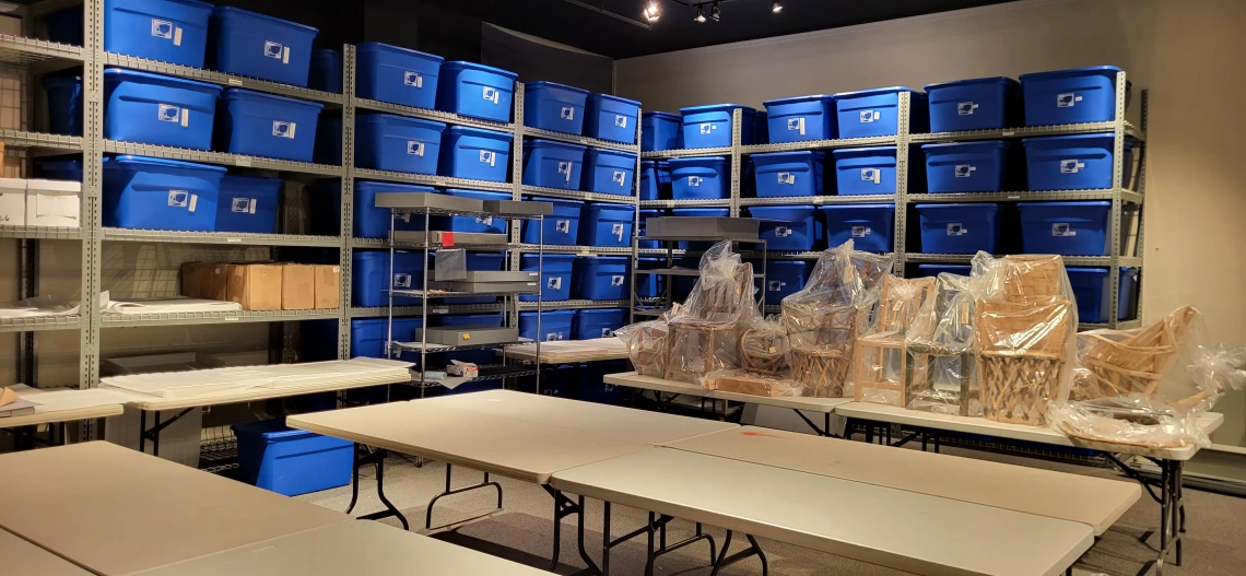 A room with shelving filled with blue tubs in the background and tables in the foreground.