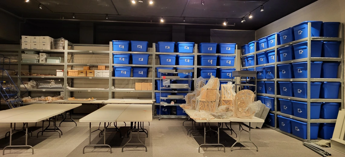 A room with shelving filled with blue tubs in the background and tables in the foreground.