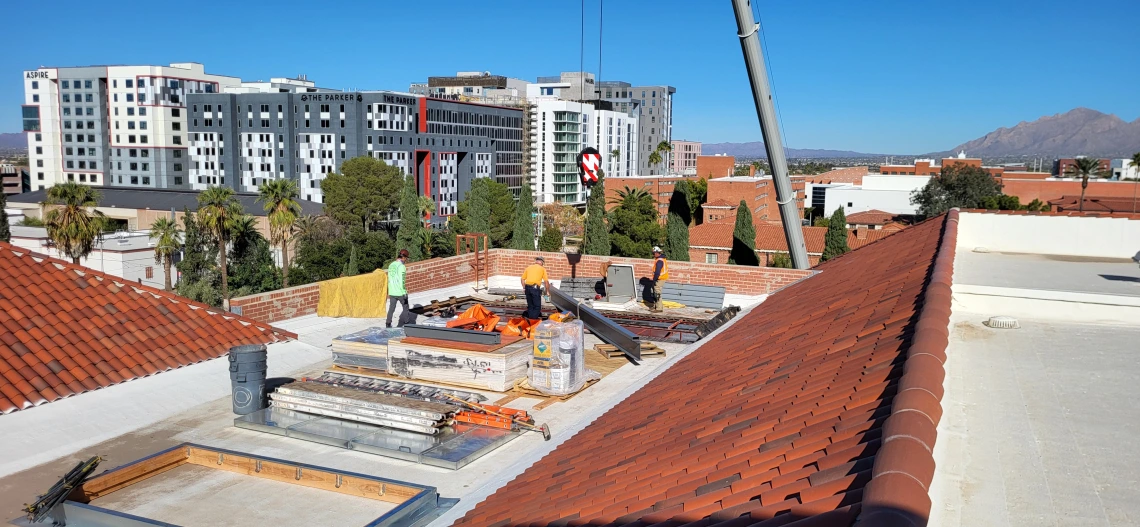 a crane is lowering a steel beam to three men on the roof the Arizona State Museum.