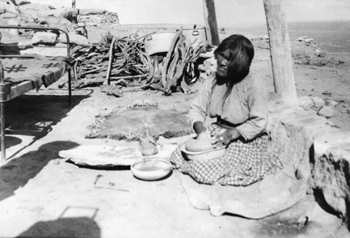 A Hopi woman sits on the ground in the beginning stages of making a pot.