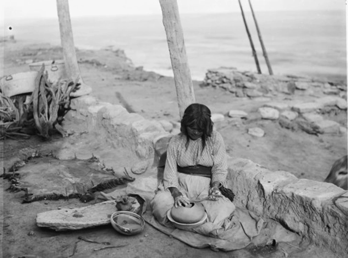 A Hopi woman sits on the ground in the beginning stages of making a pot.