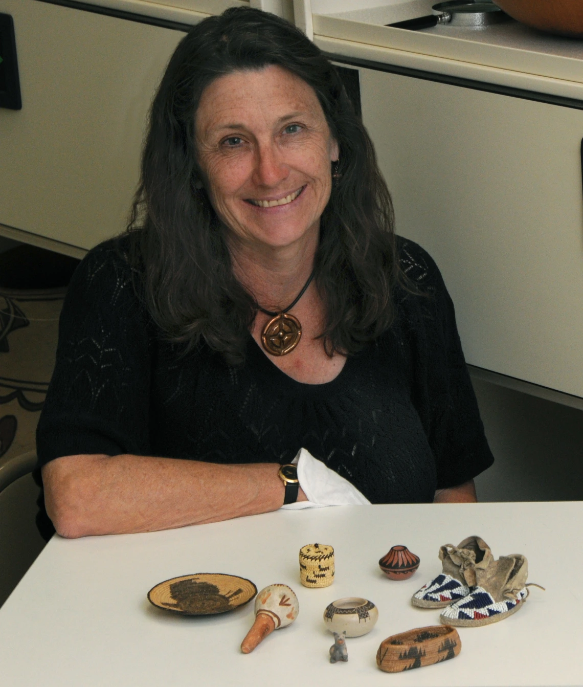 A woman sits in front of an array of miniature Native American objects from ASM collections.