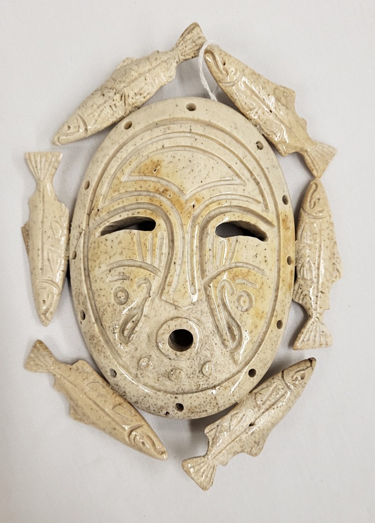 Inuit mask carved of bone, the oval face is surrounded by 6 salmon figures