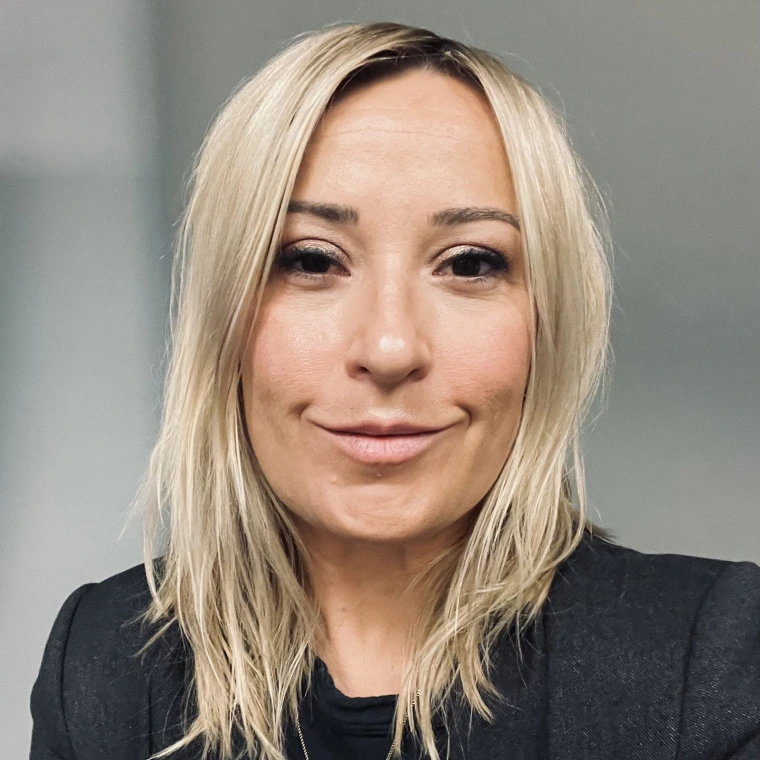a woman with straight blonde hair and wearing a dark jacket is smiling at the camera