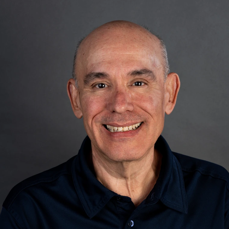 a bald man wearing a navy blue polo shirt is smiling into the camera