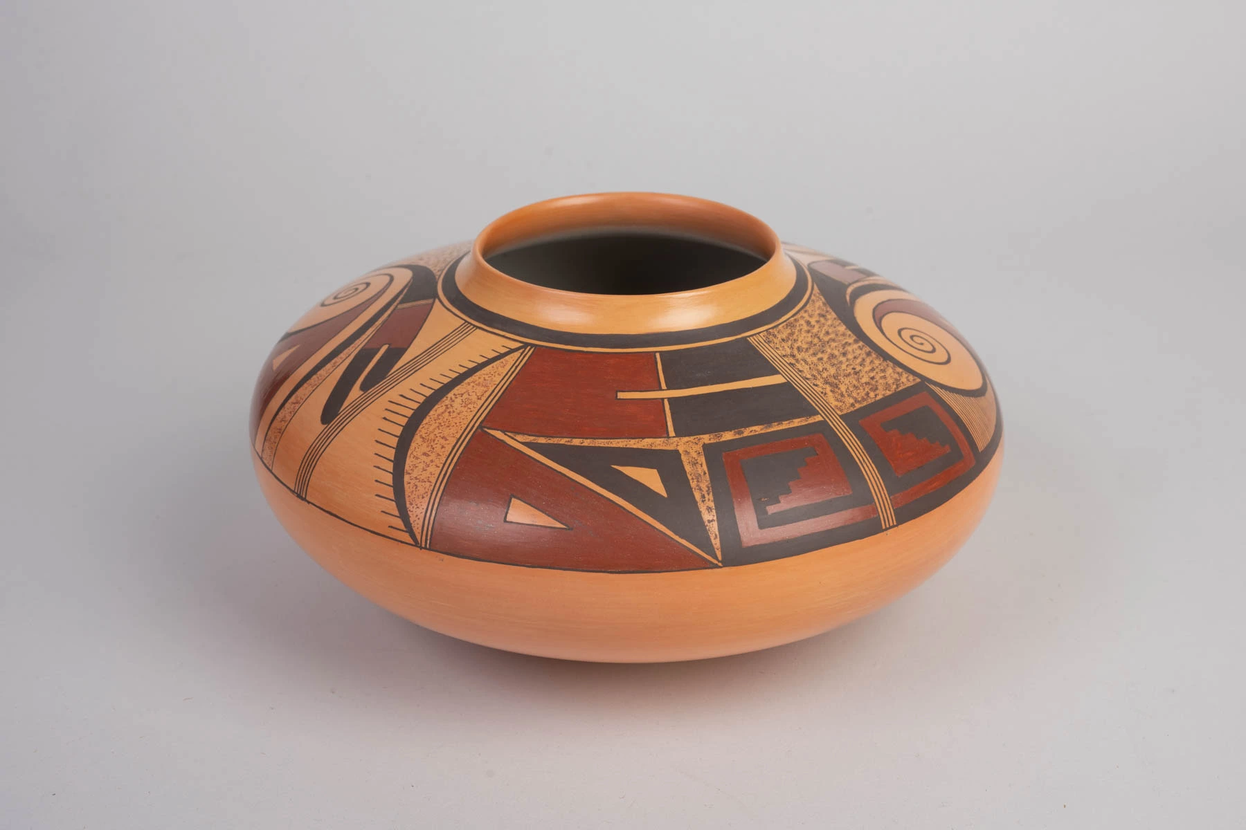 Geometrical and spiraliform designs in black and red paint on a jar of orange clay.