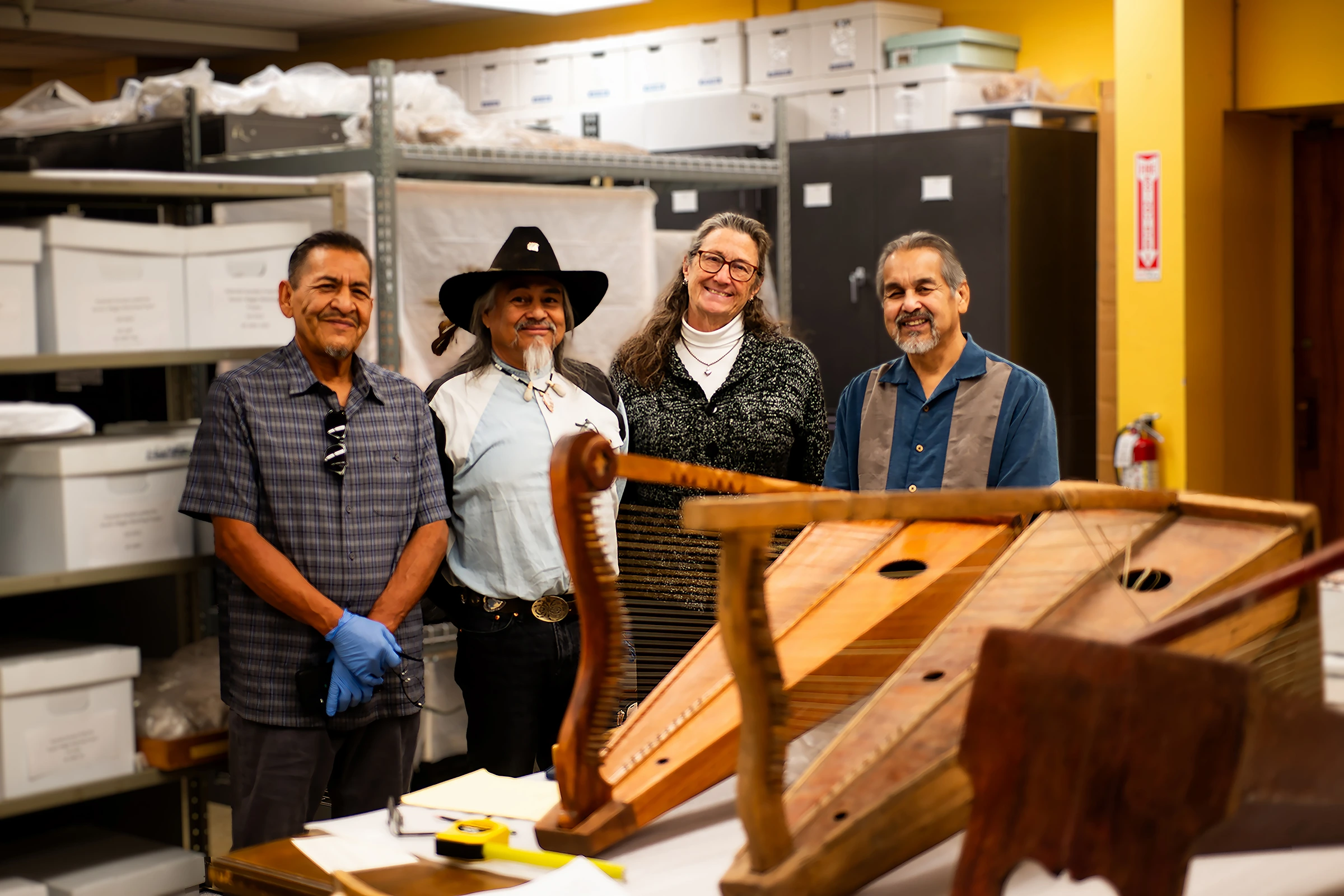 Wooden harps are in the foreground on a table. Four people, three men and one woman, stand behind the table smiling at the camera.