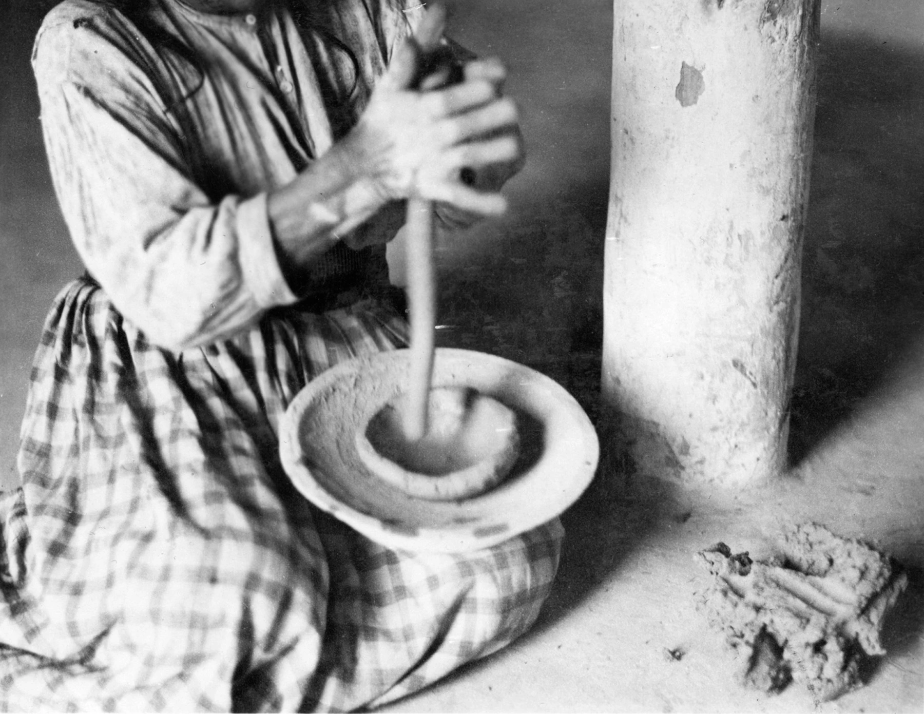 a woman makes a clay coil between her hands in order to add it to the bowl she has begun making