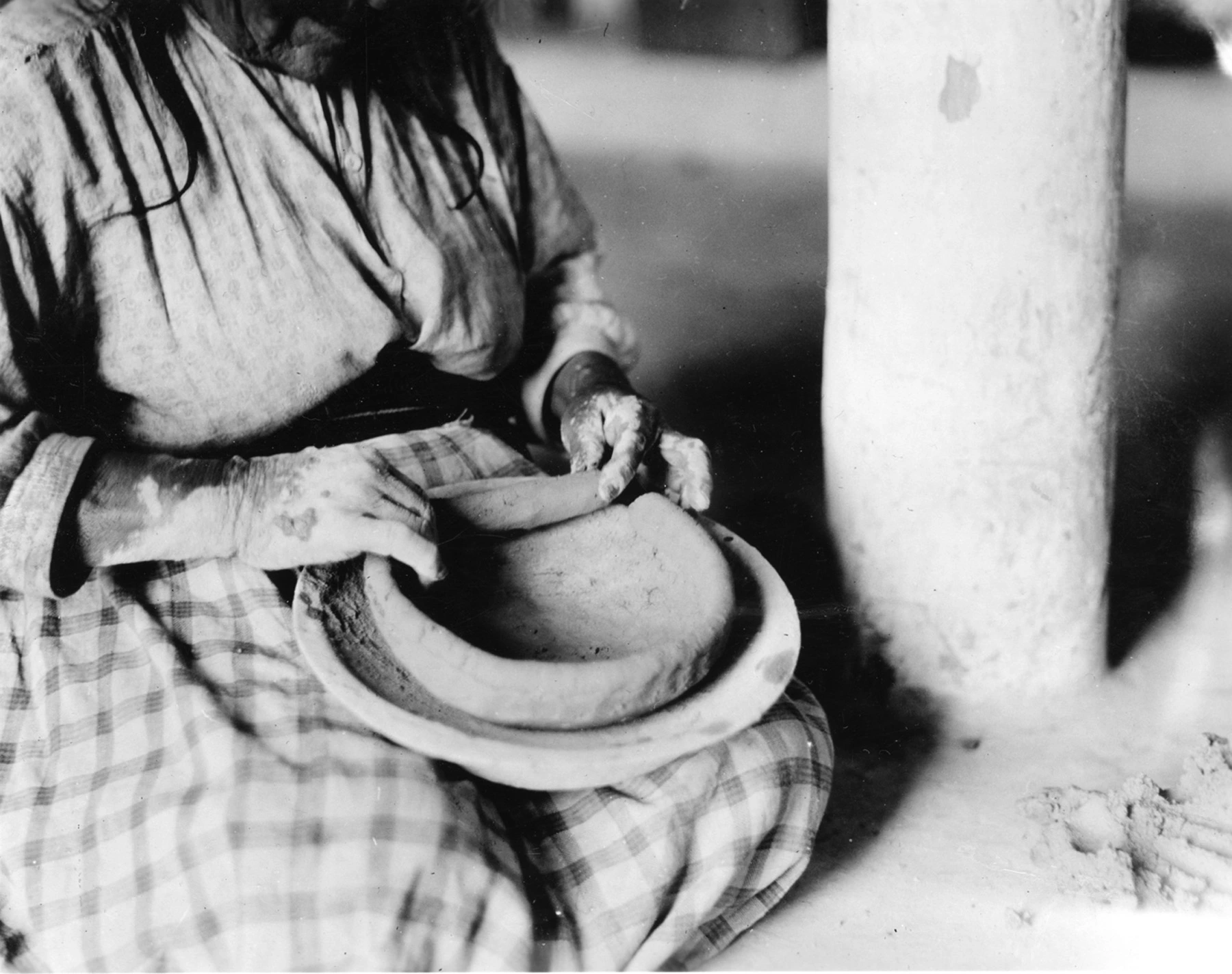 a woman adds a coil to the rim of the bowl she is making