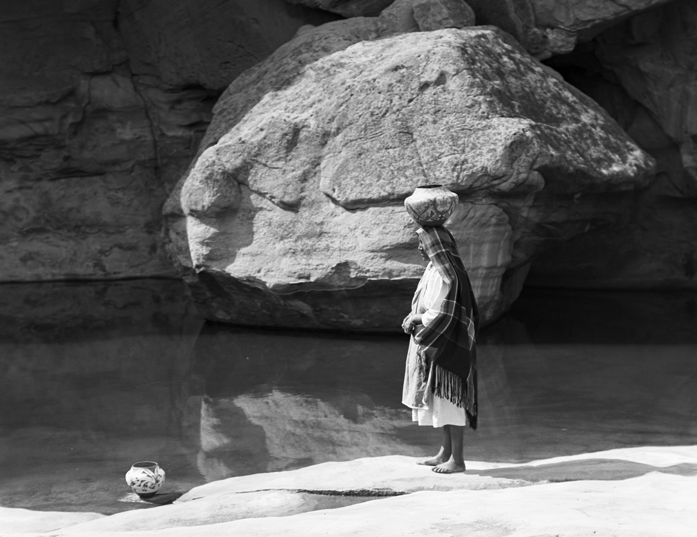 a woman balancing a canteen on her head by a body of water