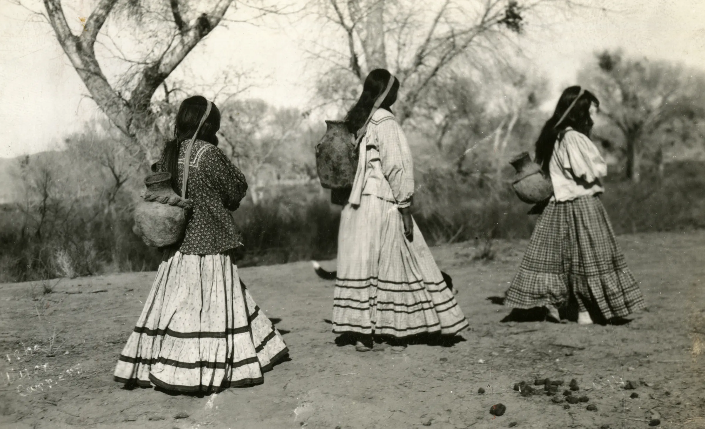 women carrying canteens strapped over their backs walking away from the camera