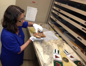 This is an image of Diane D. Dittemore, associate curator of ethnology. She is looking at beaded objects in a storage cabinet.