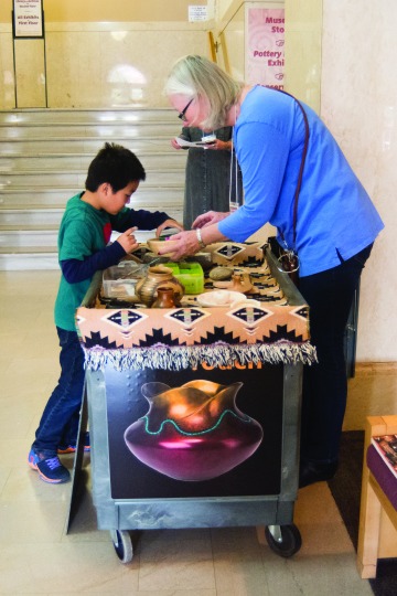 This image shows Docent Lois Eisenstein showing a boy examples of Southwest Native American pottery